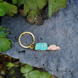 Load image into Gallery viewer, Each Happy Camper pendant measures 1.75" on the longest/widest edge and has a pink truck with a light blue trailer. Additionally is the keyring and one jump ring.
